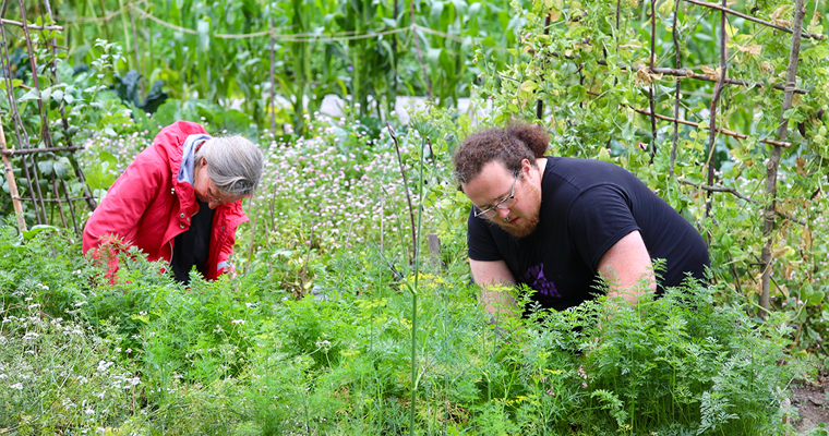 Två studerande sitter på huk i en rabatt.
